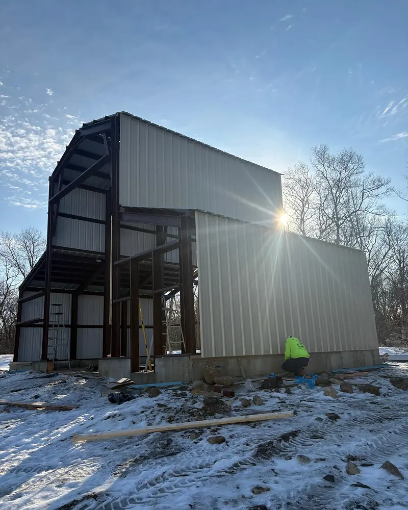 Steel building under construction in winter, with a crew member at work